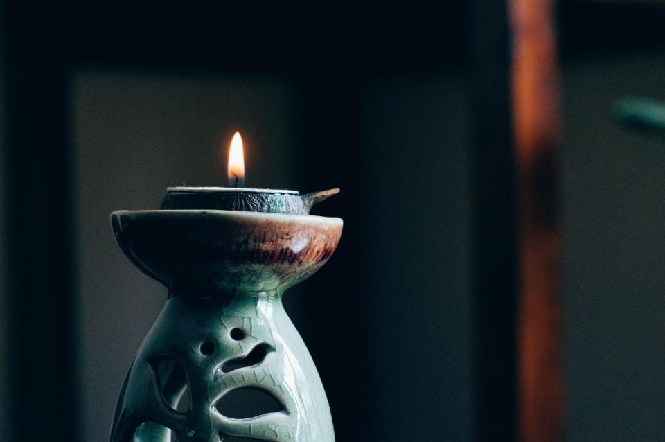 A lit candle in a glazed ceramic holder, against a dark background.